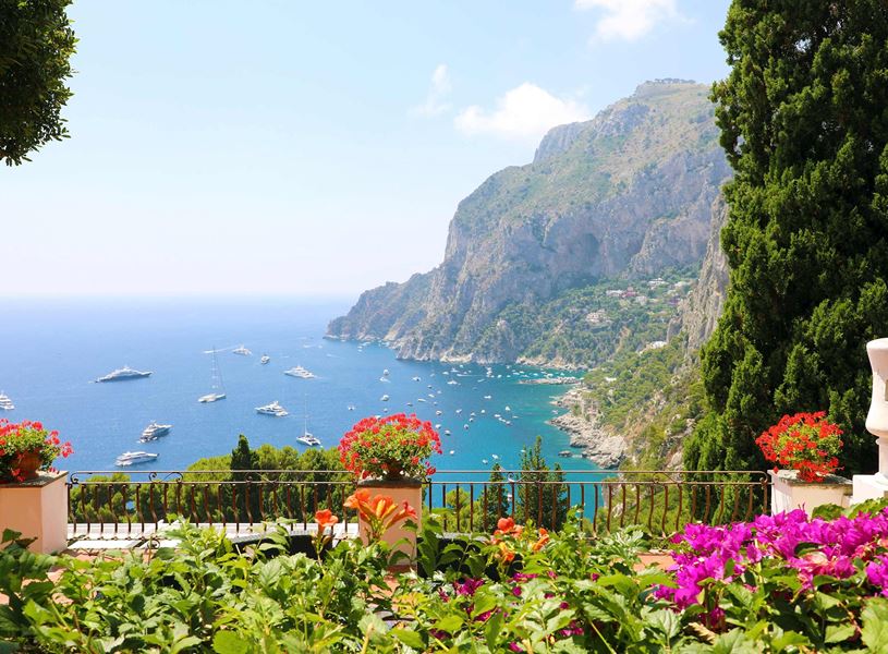 Colourful garden terrace overlooking Capri coastline with yachts on blue sea