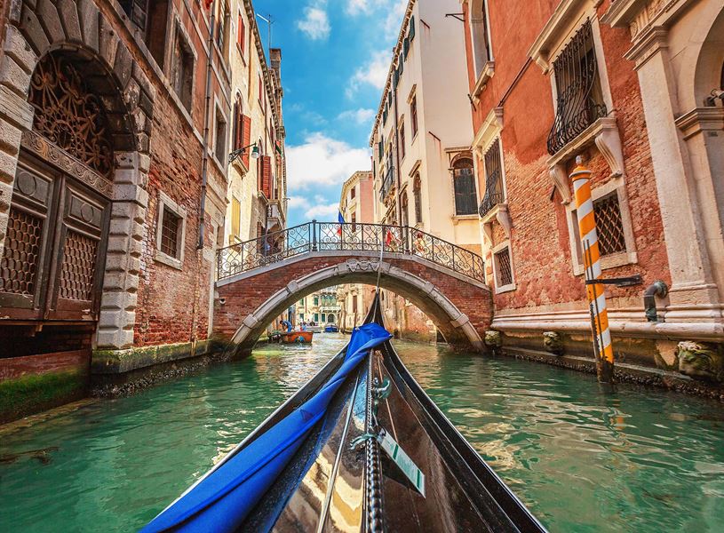 Gondola approaching iron bridge on Venetian canal with historic building