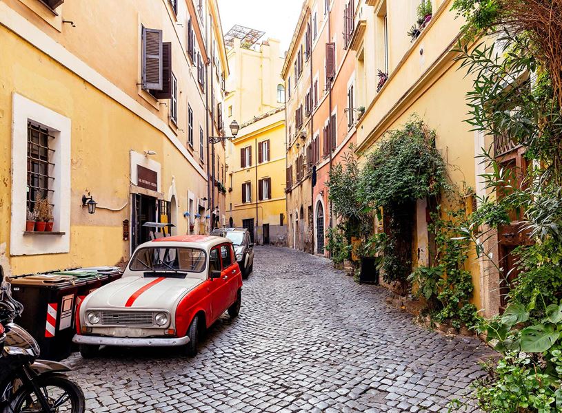 Vintage red car parked on narrow cobblestone street lined with colourful buildings 