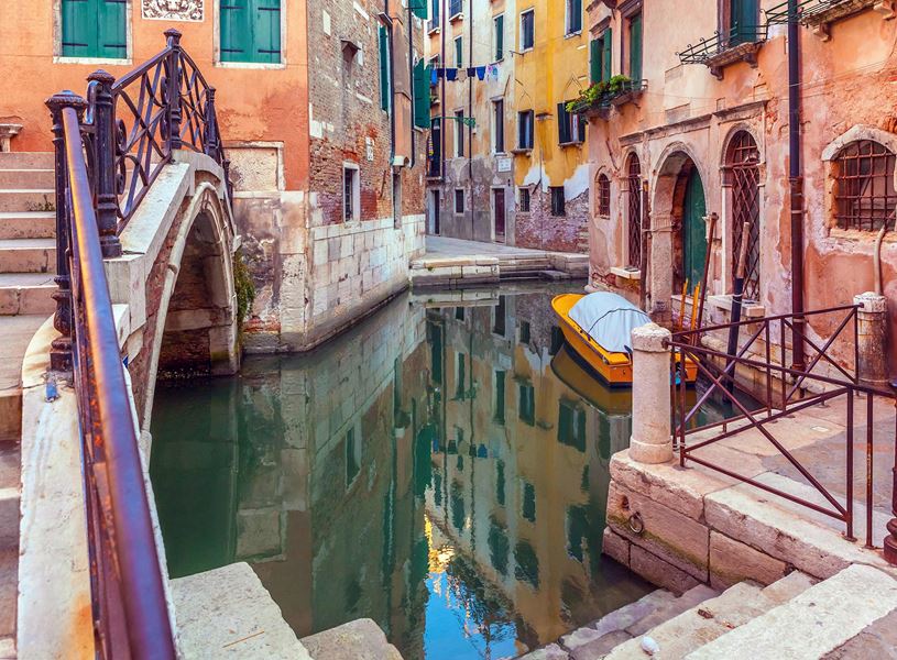 Colourful Venetian canal with arched stone bridge, moored yellow boat
