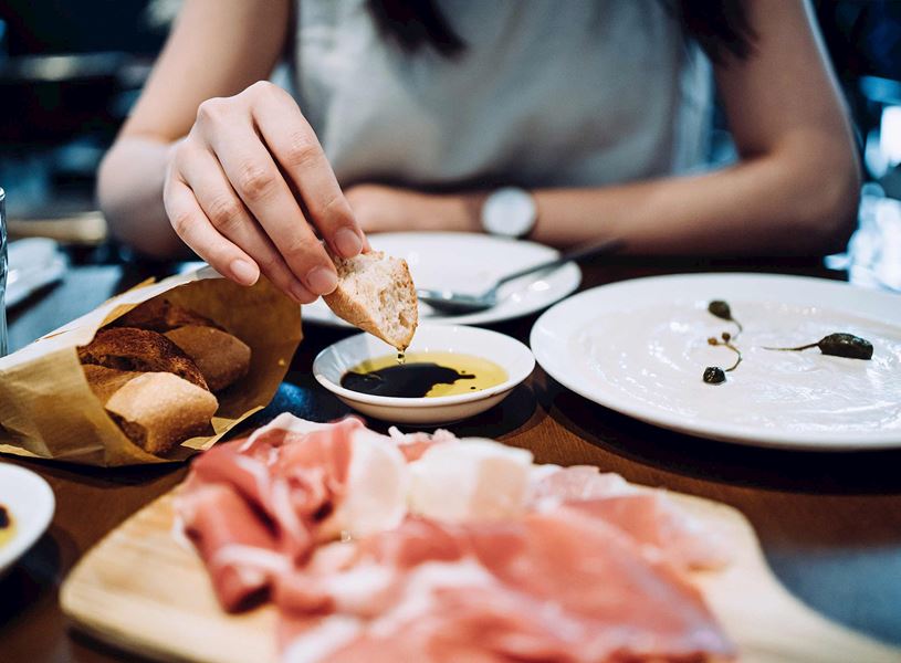 Hand dipping bread into olive oil beside cured meats and plates