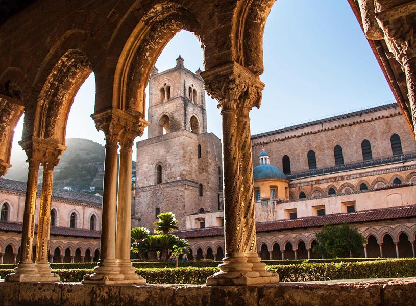 View of Cathedral of Monreale courtyard through ornate arches with tower and garden