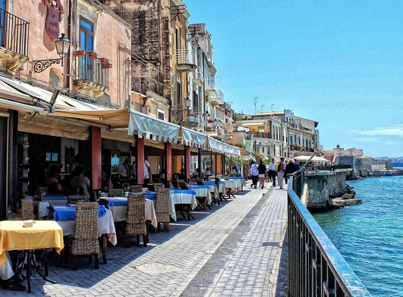 Outdoor waterfront restaurant in Syracuse along stone-paved promenade by the sea