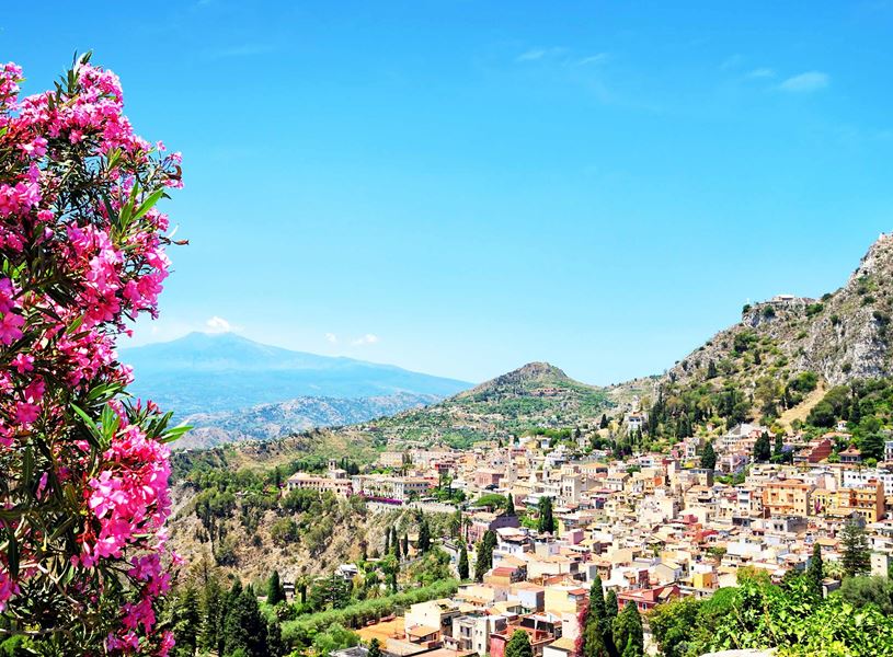 Panoramic view of Taormina in Sicily with pink flowers and Mount Etna in background
