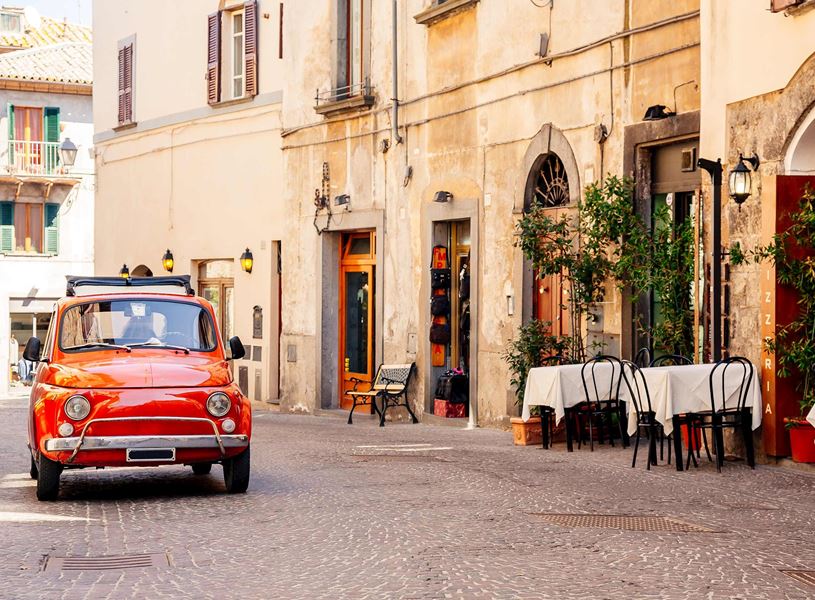 Vintage red car parked on cobblestone street beside outdoor tables