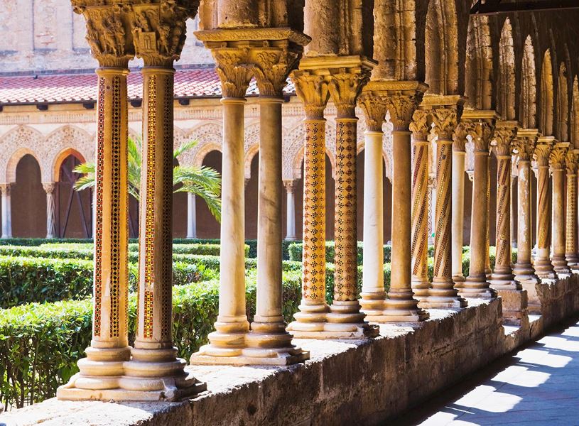 Row of intricately carved columns in Cathedral of Monreale cloister with garden view