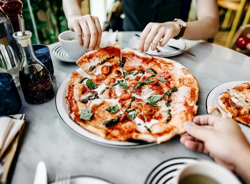 Hands reaching for slices of Margherita pizza topped with basil and cherry tomatoes 