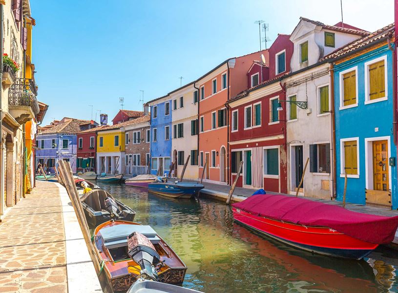 Colourful houses along canal with moored boats and stone walkway in Burano, Venice 