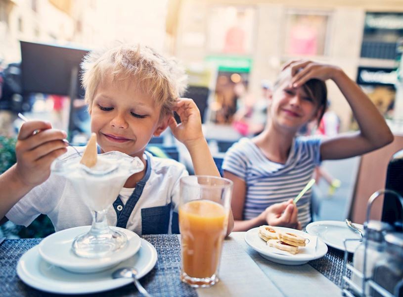 Two children sitting at outdoor cafe table with glass of juice and ice cream