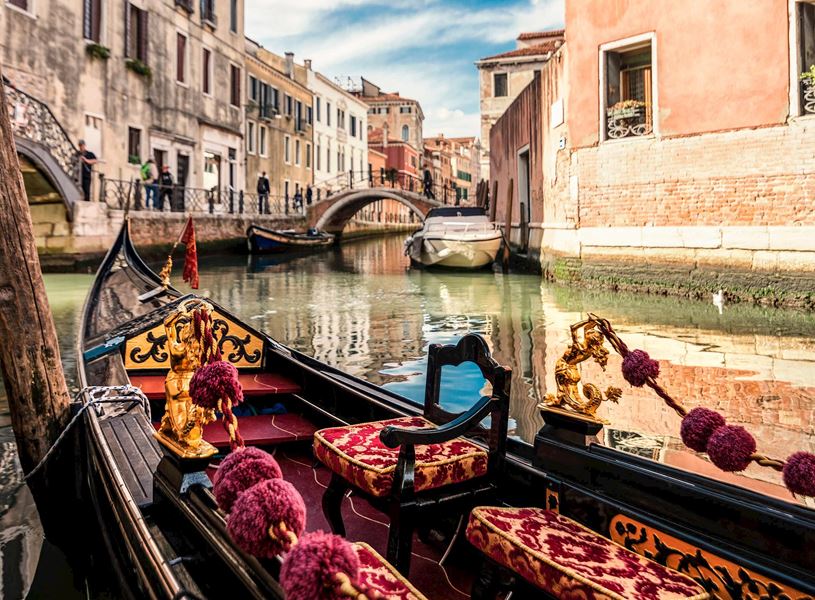 Gondola with velvet seats and golden decorations on Venetian canal near stone bridge