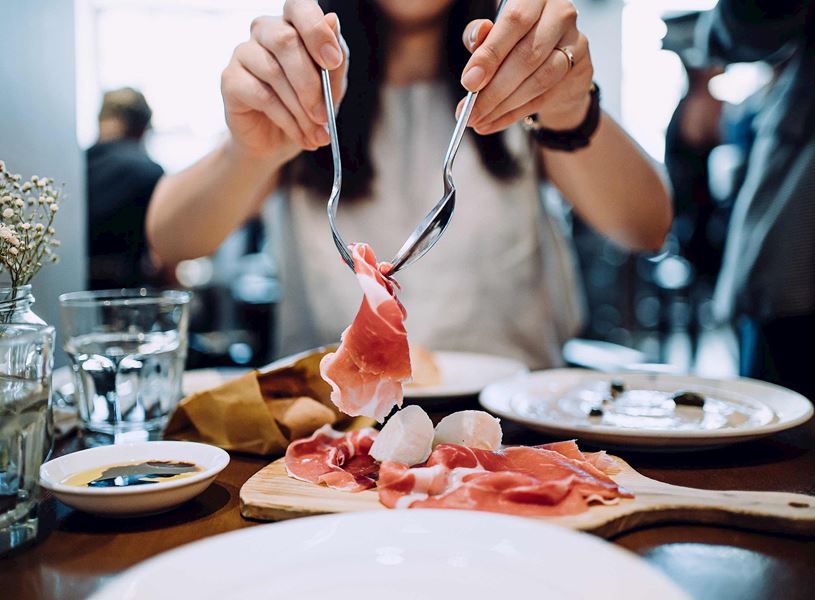 Close-up of hands serving slices of prosciutto with mozzarella on wooden board
