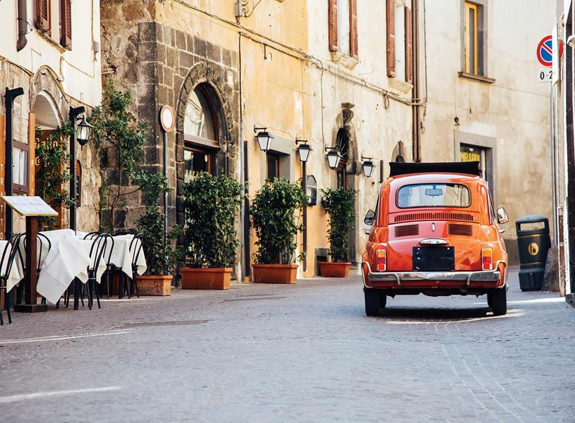 Vintage red car parked on cobblestone street beside outdoor tables