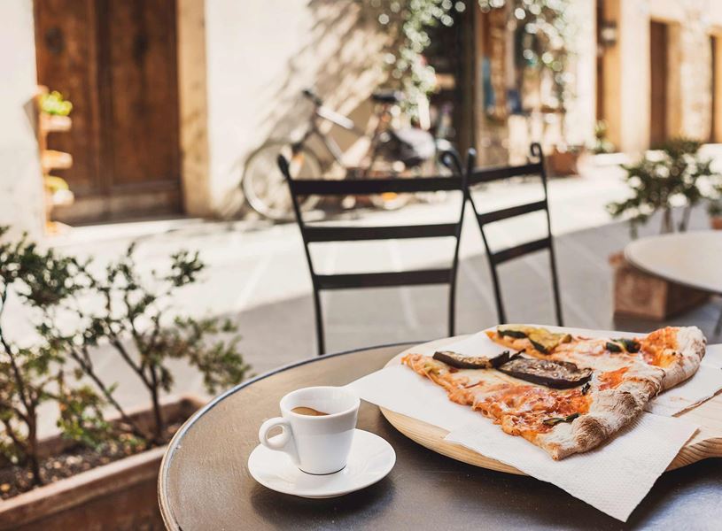 Slices of Italian pizza with grilled vegetables on wooden board beside espresso cup outdoors