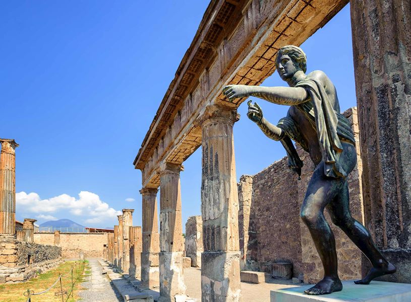 Bronze statue at Temple of Apollo in Pompeii with ancient stone columns and ruins