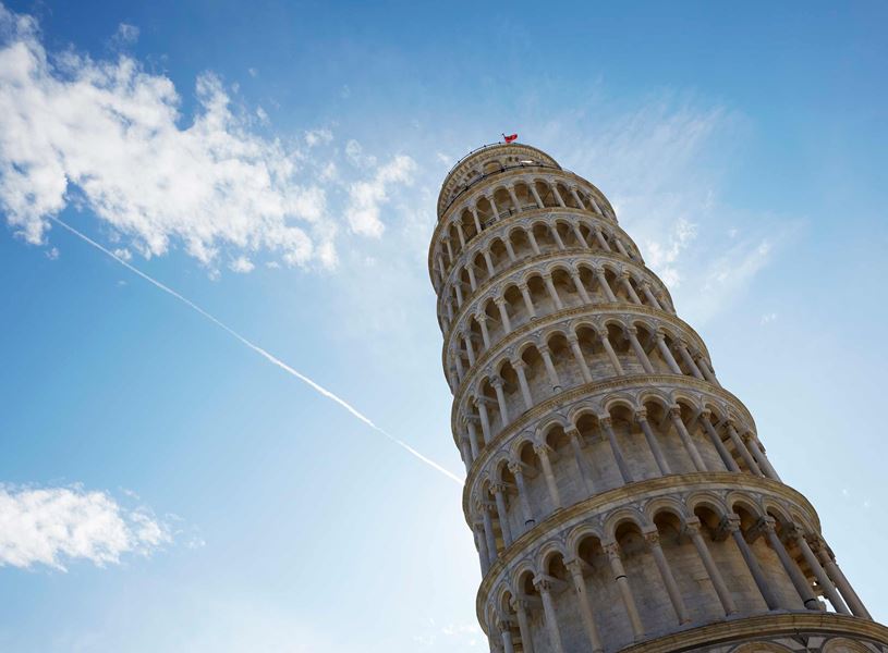 Leaning Tower of Pisa against bright blue sky with scattered clouds and contrail