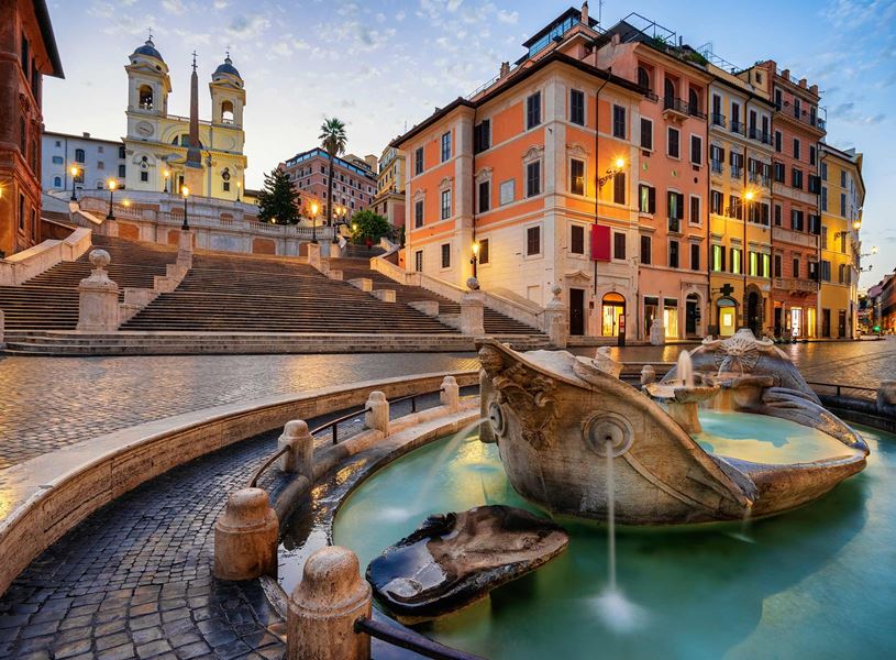 Barcaccia Fountain at Spanish Steps in Rome with illuminated buildings and Trinità dei Monti church