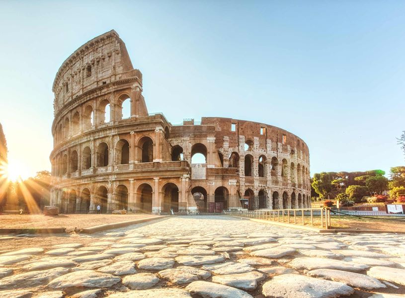 Colosseum in Rome at sunrise with sunburst effect and cobblestone foreground walkway