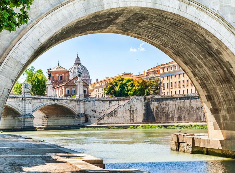 St. Peter’s Basilica dome framed by stone bridge arch over Tiber River in Rome
