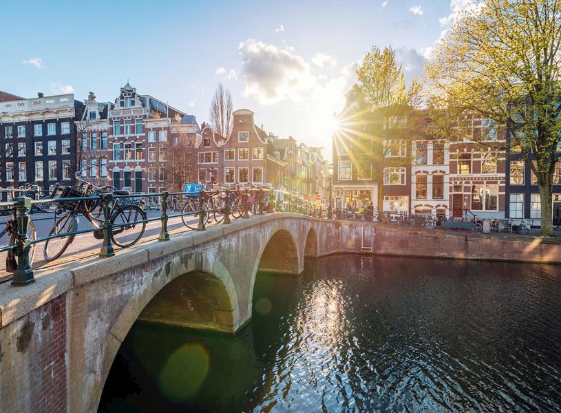 Amsterdam canal with arched stone bridge, bicycles and buildings