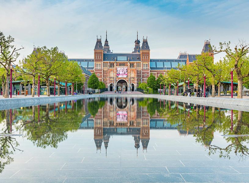 Rijksmuseum in Amsterdam with symmetrical reflection in long water feature surrounded by trees