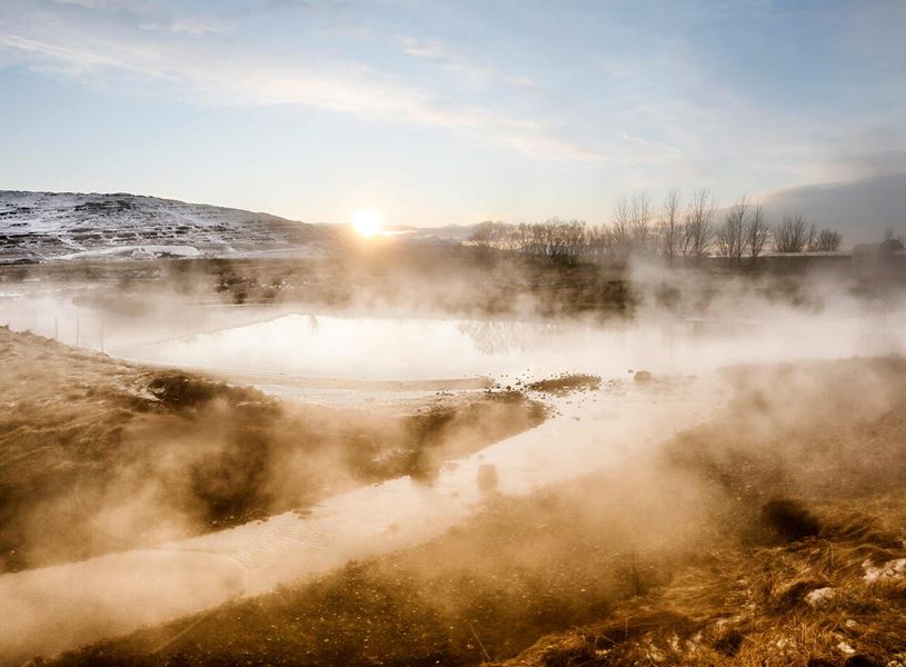 Deildartunguhver hot spring with rising steam and snowy hill backdrop