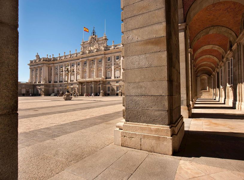 Royal Palace of Madrid with Spanish flag and stone archway corridor