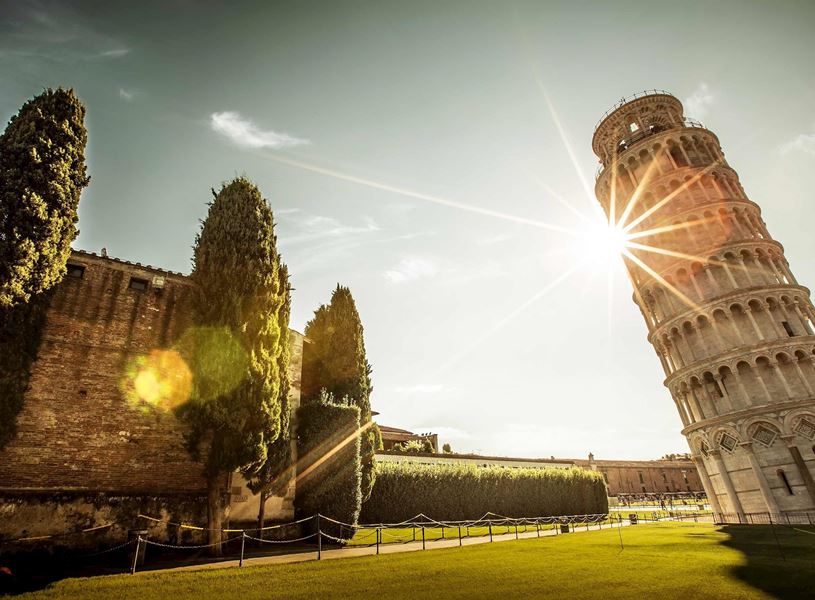 Leaning Tower of Pisa with sunburst effect and tall cypress trees in foreground