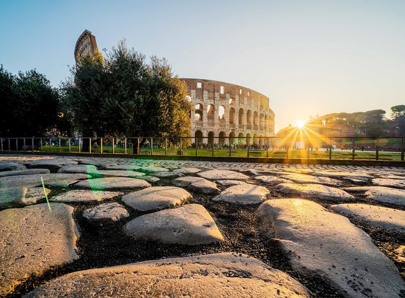Colosseum in Rome at sunrise with sunburst effect and ancient cobblestone foreground