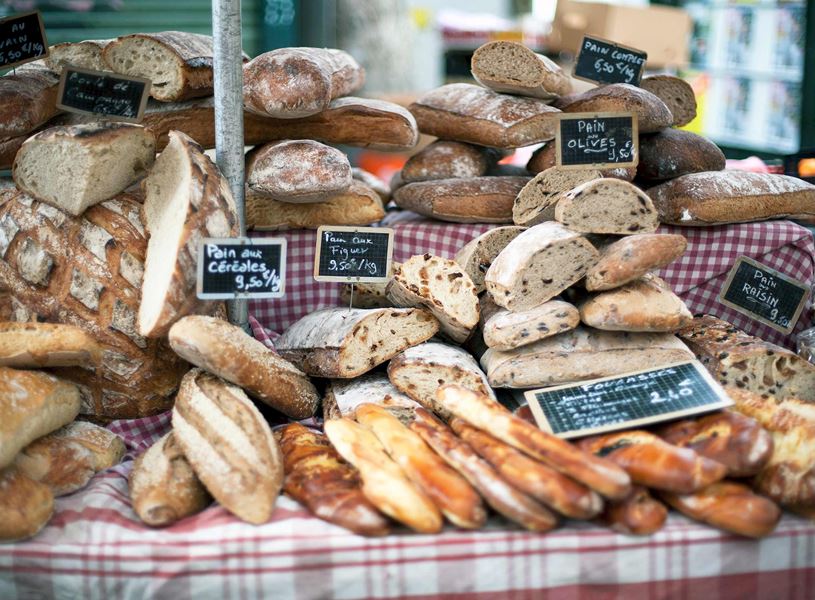 Rustic bakery table with assorted breads and handwritten sign on checkered cloth