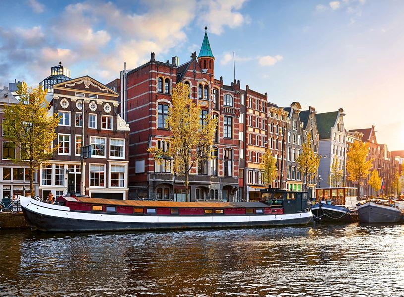 Houseboat moored along Amsterdam canal with buildings and autumn trees 