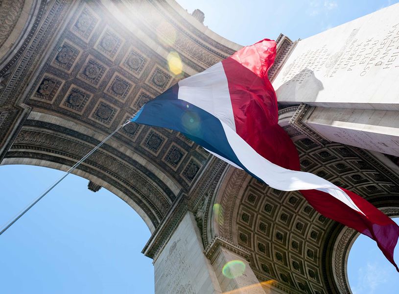 French flag waving under Arc de Triomphe and inscriptions in Paris, France