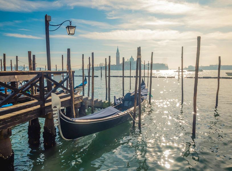 Gondola moored at wooden dock in Venice with lampposts and San Giorgio Maggiore church across shimmering water