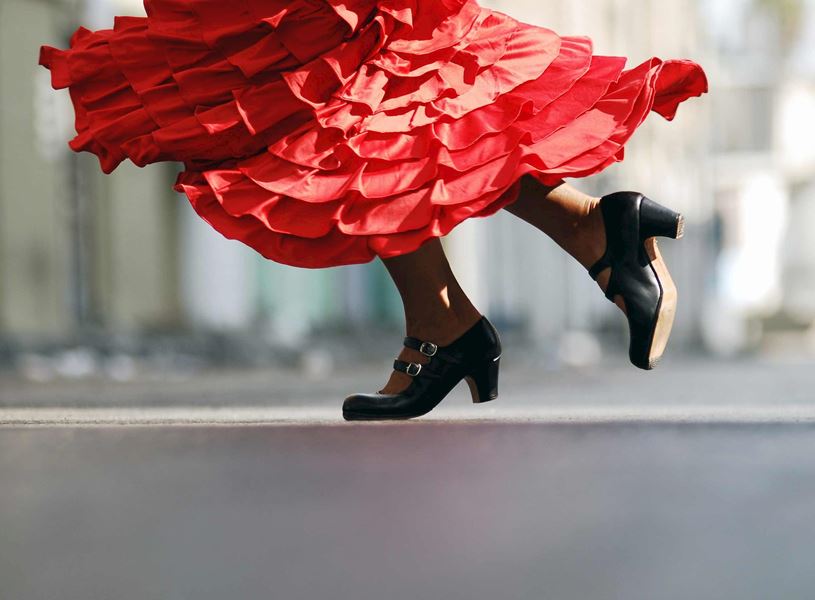 Close-up of flamenco dancer’s black shoes and flowing red ruffled dress mid-step