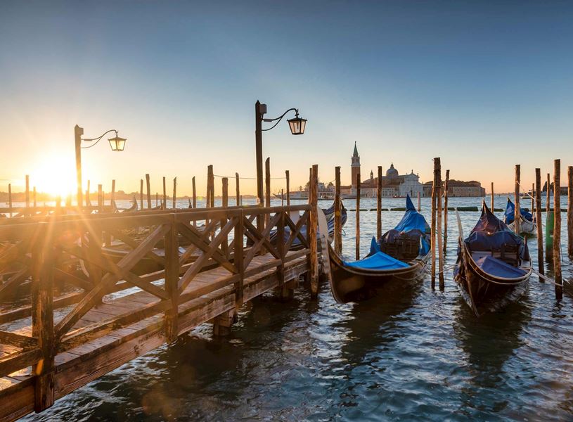 Gondolas moored at wooden dock in Venice with lampposts and San Giorgio Maggiore church at sunrise