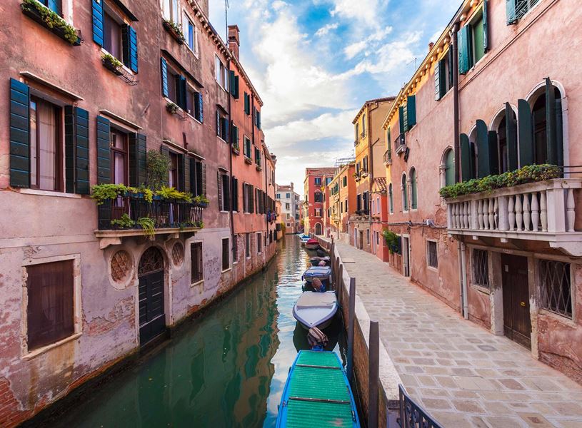 Narrow Venetian canal lined with buildings featuring green shutters and moored boat