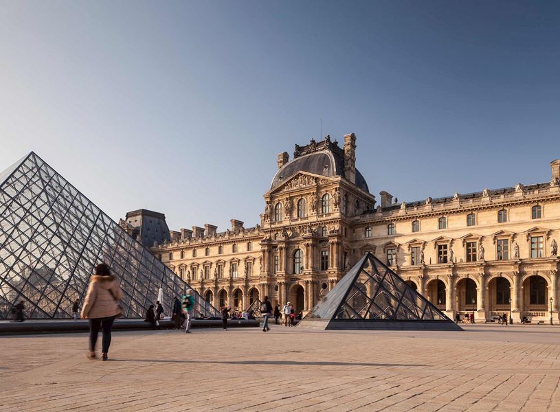Louvre Museum glass pyramids with historic architecture and visitors in courtyard