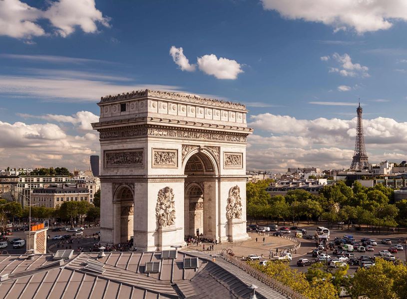Arc de Triomphe with Eiffel Tower in background and busy roundabout in Paris, France
