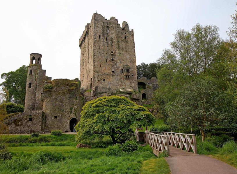 Blarney Castle tower with wooden bridge surrounded by greenery in Ireland