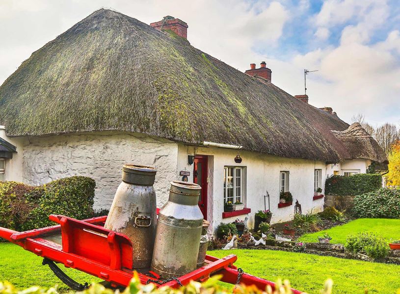 Thatched cottage with milk churns outside in Adare, Ireland