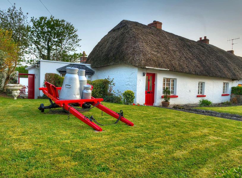 Thatched cottage with red cart and milk churn outside in Adare, Ireland
