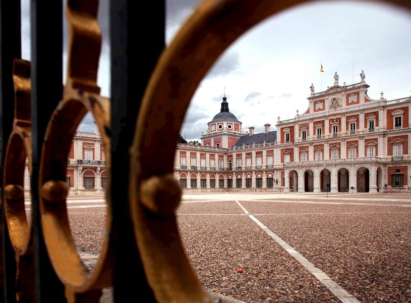 Royal Palace of Aranjuez viewed through iron gate with gravel courtyard in Spain