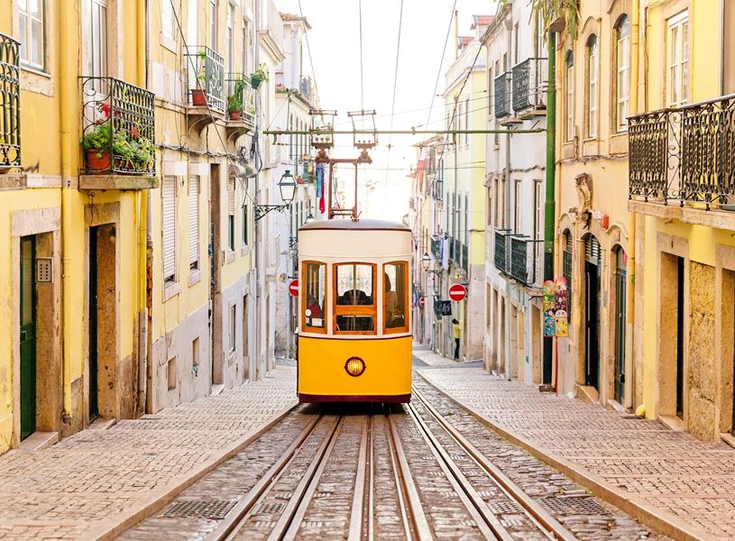 Yellow tram on steep cobblestone street in Lisbon’s historic district