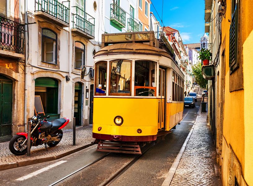 Yellow tram passing narrow cobblestone street in Lisbon’s old town
