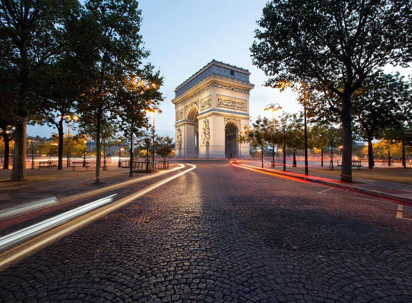 Arc de Triomphe at twilight with light trails and tree-lined street in Paris, France