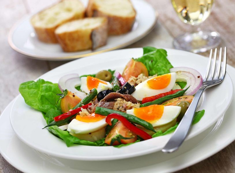 Niçoise salad on a plate with eggs, tuna, vegetables and bread