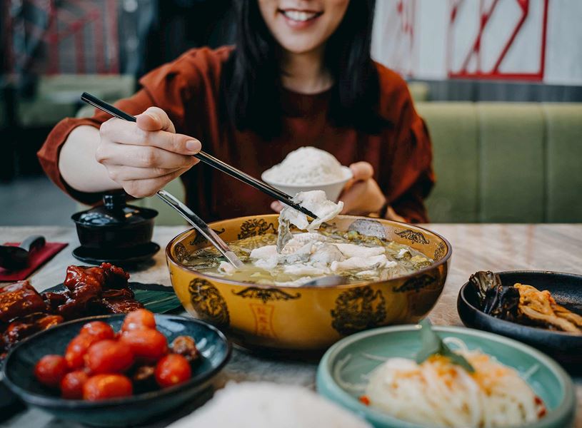 Smiling woman enjoying Szechuan dishes including boiled fish in restaurant, China