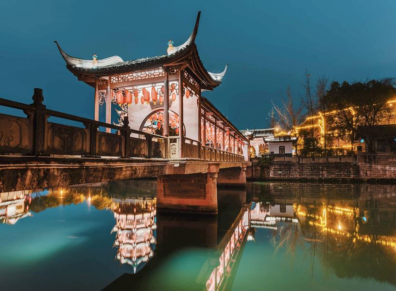 Illuminated Baihuatan traditional bridge reflected in water at night, Chengdu, China