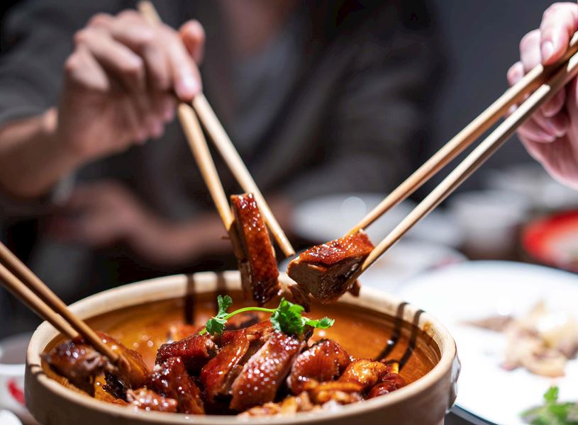 Three pairs of chopsticks picking chicken from shared dish, Beijing, China
