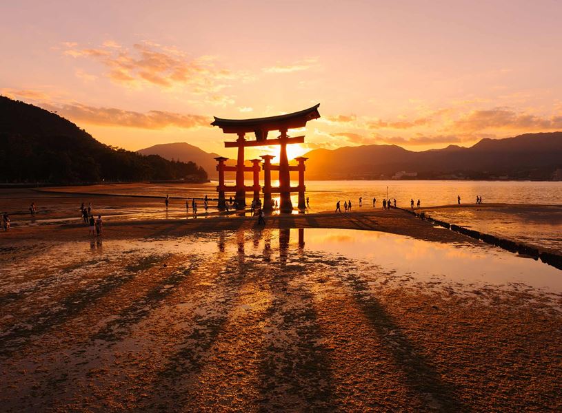 Sunset behind Itsukushima Shrine torii gate on tidal flats, Hiroshima, Japan