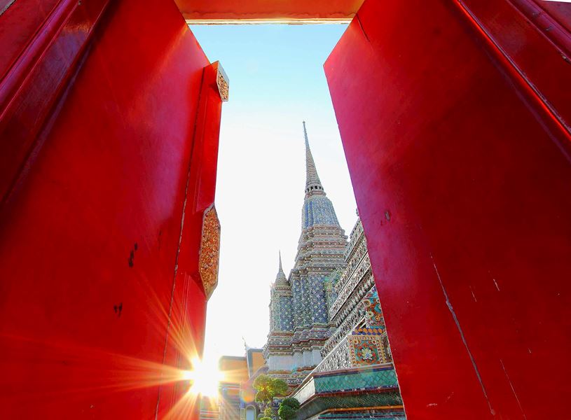 View of Wat Pho temple spire framed by red doorway panels, Bangkok, Thailand